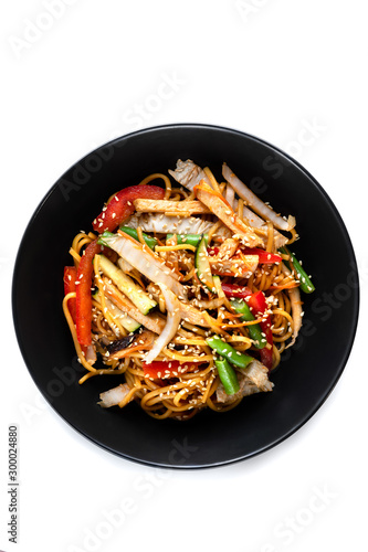 Sliced grilled chicken breast, noodles in sauce, vegetables and sesame seeds in a black plate isolated on white background