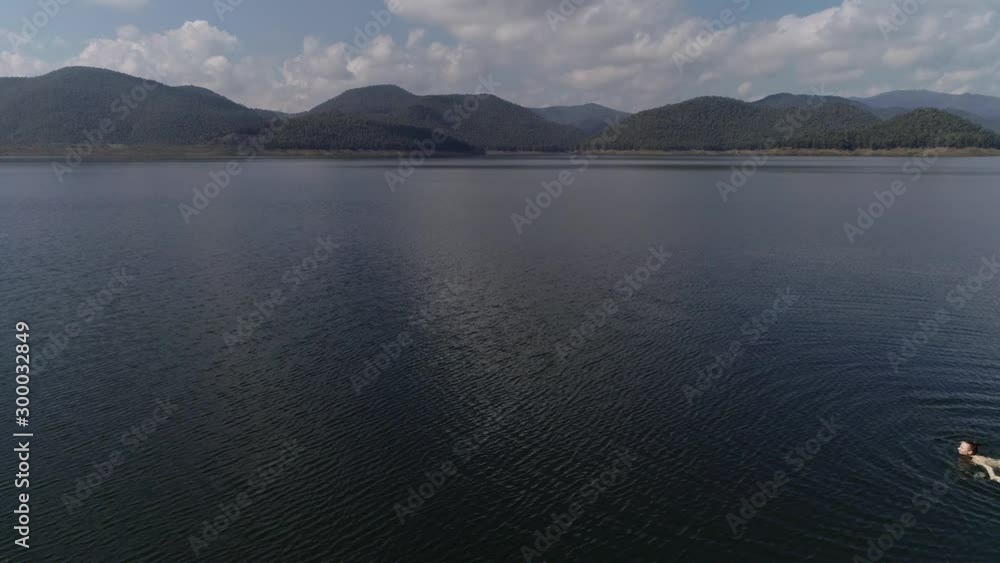 Sexy slim woman is floating on the water. The general plan from afar. Aerial photo on a mountain lake. beautiful young girl lies on a mattress in the open sea or in the pool, a pink bikini, hat Sexy slim woman is floating on the water. The general plan from afar. Aerial photo on a mountain lake. beautiful young girl lies on a mattress in the open sea or in the pool, a pink bikini, hat