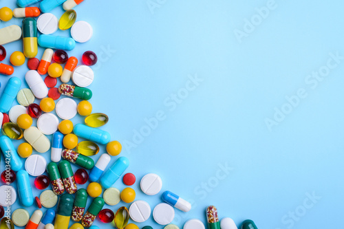 Medicine background of capsules pills of different size, color on light blue table. Concept of treatment, illness.