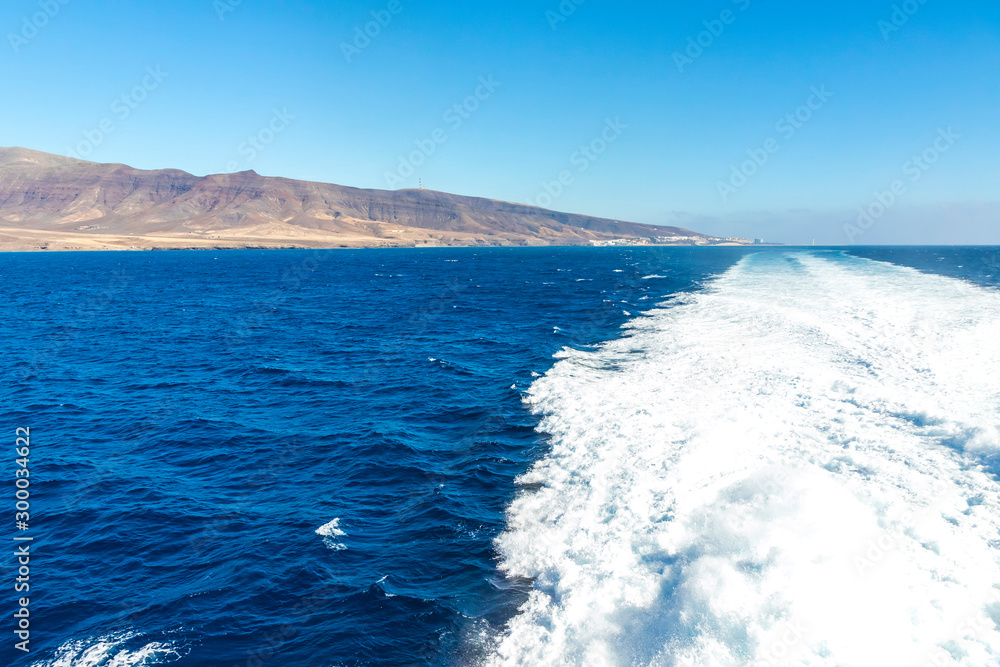 Water trail foaming behind a ferry boat in Atlantic ocean between Canary islands, Spain. Fuerteventura island on the background