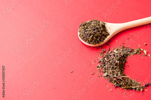 Spices: dried Basil grass on wooden boat on red background