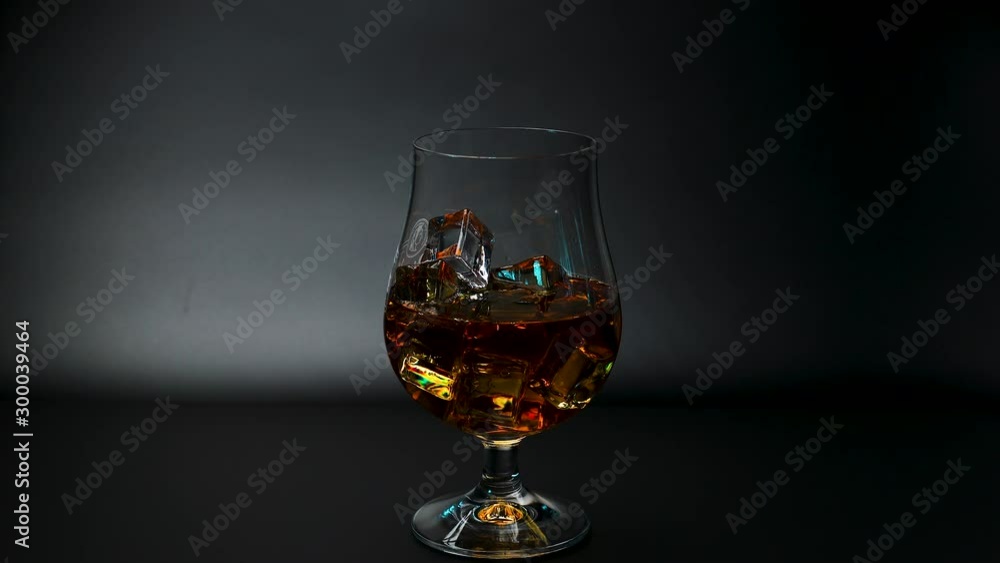 Short film showing whiskey being poured into a tulip glass with ice on black background. Slow motion. Beautiful backgrounds. Alcohol concept. Short film showing whiskey being poured into a tulip glass with ice on black background. Slow motion. Beautiful backgrounds. Alcohol concept.