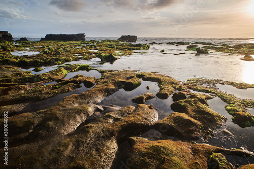 Bali island landscape sunset seaside view. Rock with seawead and black sand in long exposure photo