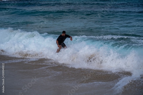 Young man riding a wave on a skimboard (a mix of surf and skate) in Cala Mesquida (Mallorca, Spain)