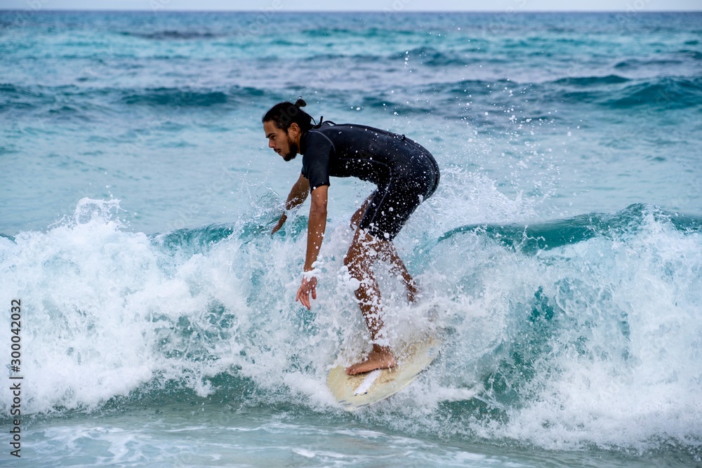 Young man riding a wave on a skimboard (a mix of surf and skate) in
