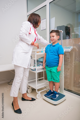 Female doctor measuring the height of little boy in a clinic ( hospital ) while smiling and being gentle.