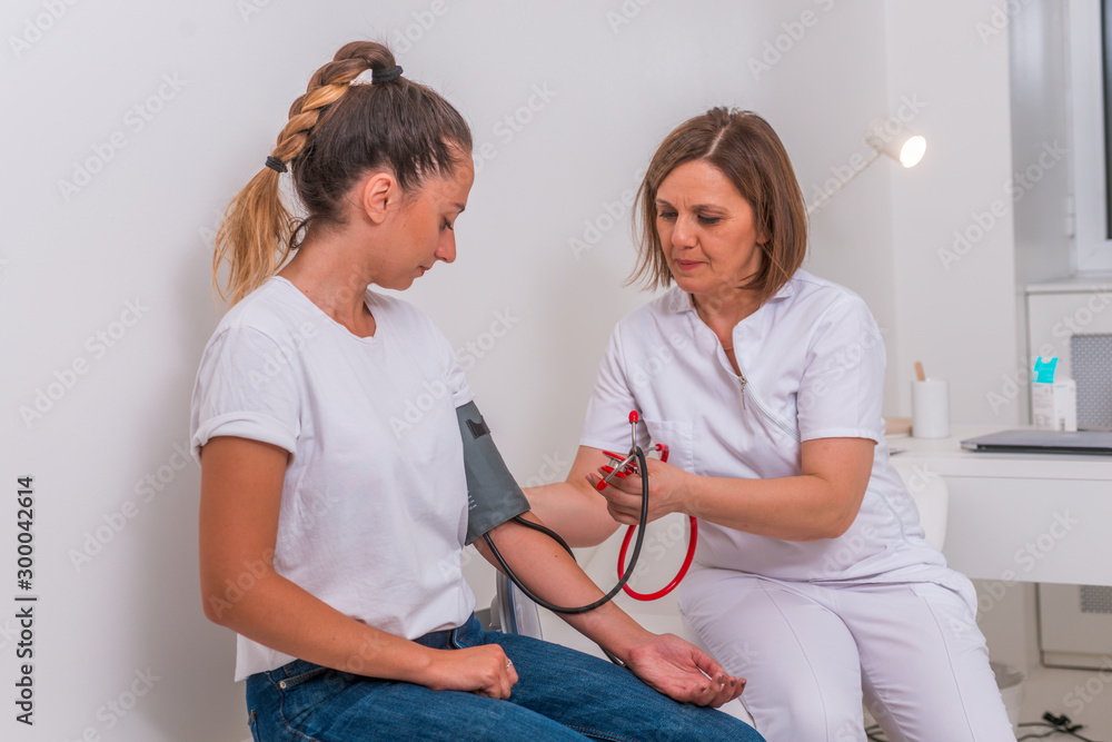Female doctor measuring the blood pressure of her young teen patient ...
