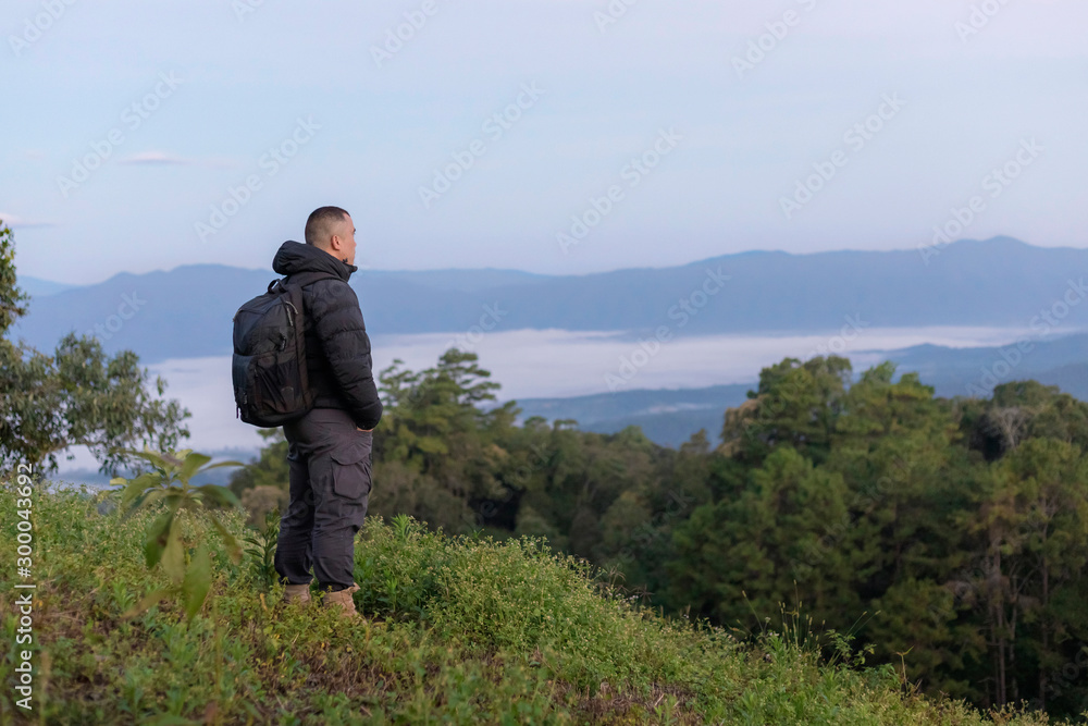 male tourist with backpacks stand to the top of mountain and enjoying sunrise and mist.