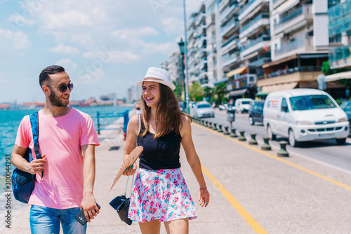 Cute couple walking by the sea on a boardwalk while the girl holds a palette and smiles to her boyfriend.