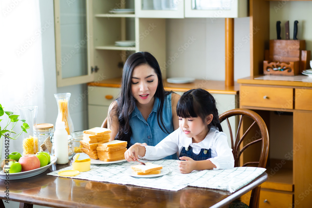 Mother and child daughter Spread butter on bread in the morning. happy family in the kitchen Mother and child daughter Spread butter on bread in the morning. happy family in the kitchen