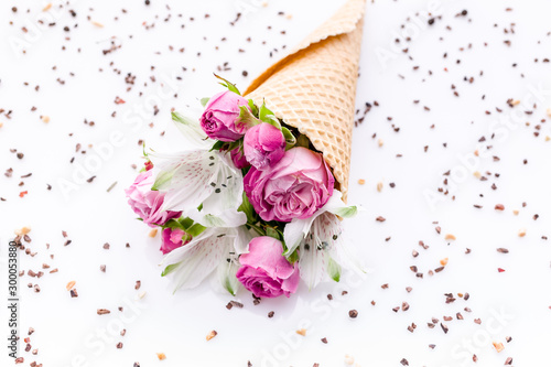 Bouquet of flowers in a waffle cone on a chocolate chip pattern. Rose and alstrameria on a white background. Theme for greeting cards or wedding invitations. photo