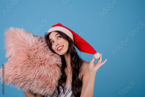 woman with pink fluffy pillow wearing santa hat isolated over blue photo