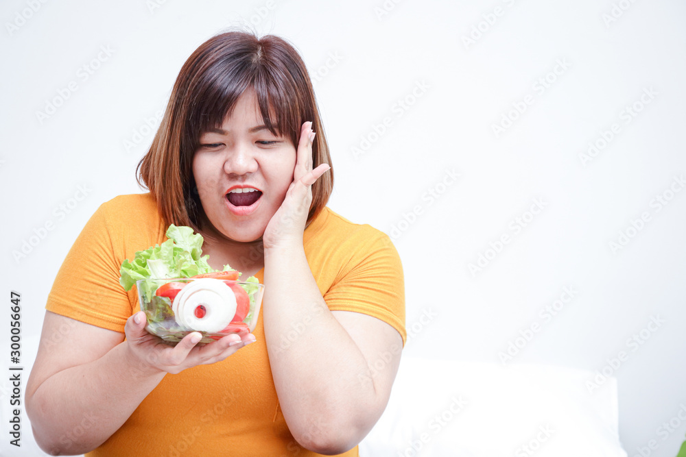 Fat Asian women eat fresh vegetables to lose weight. At the bed in her room Fat Asian women eat fresh vegetables to lose weight. At the bed in her room
