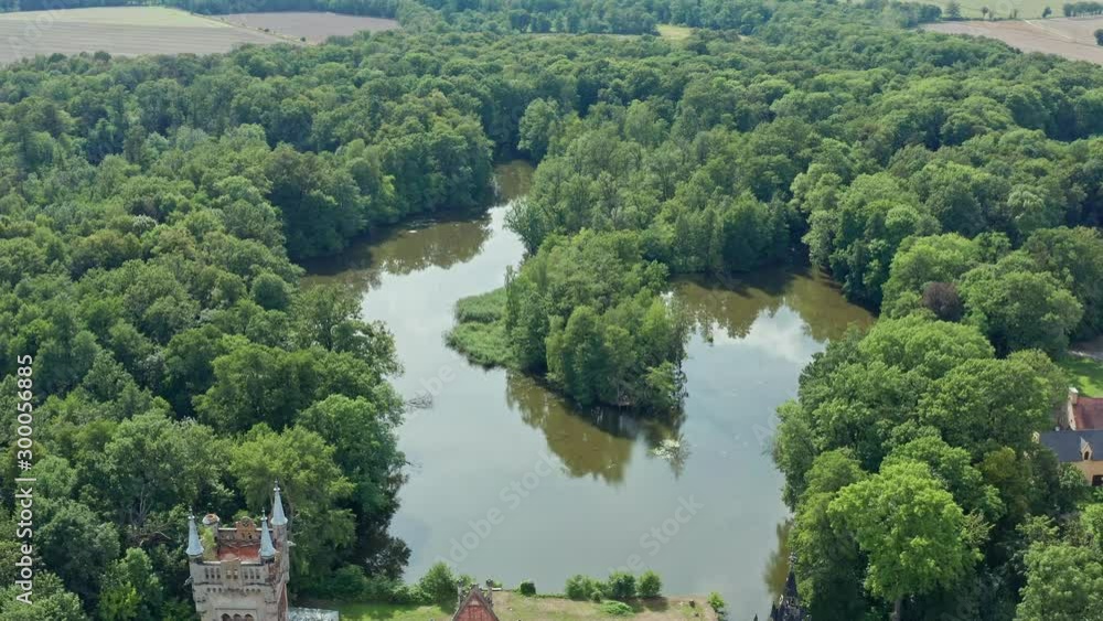 Drone aerial shot over a lake surrounded with trees and marsh land revealing a stunning old castle ruins
