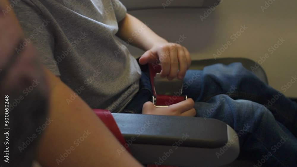 Close-up of a small child unbuckles seat belts in an airplane. A little boy sits in a chair on the plane and fastens his seat belt. A small child indulges in an airplane with a seat belt. Close-up of a small child unbuckles seat belts in an airplane. A little boy sits in a chair on the plane and fastens his seat belt. A small child indulges in an airplane with a seat belt.