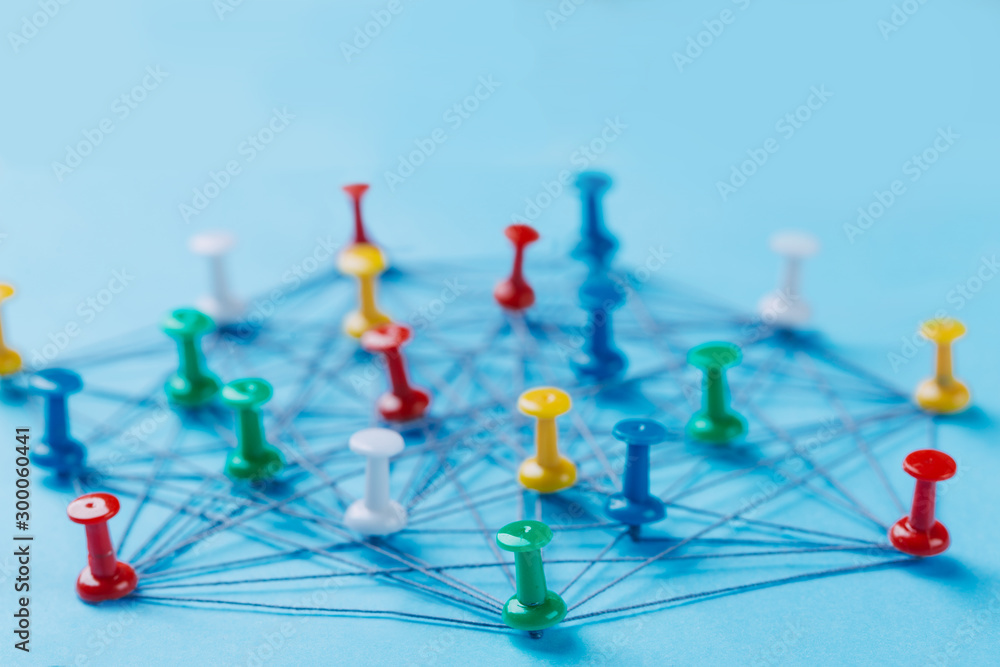 © Nana_studio - Small network of colorful pins and string, An arrangement of colorful pins linked together with string on a blue background suggesting a network of connections.