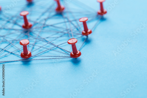 network with red pins and string, An arrangement of colorful pins linked together with string on a blue background suggesting a network of connections.
