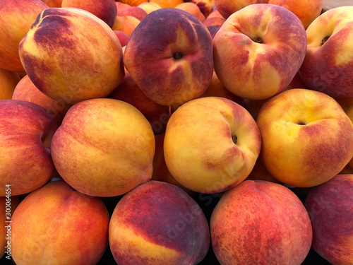 Close up on display of yellow peaches, quintessential peach. They are distinguished by their fuzzy thin skin with hues of red, pink and gold blushing throughout.