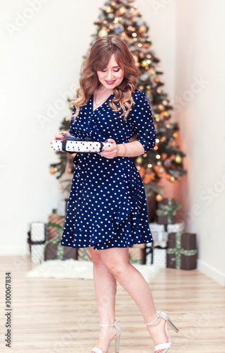 Beautiful girl in a blue dress with a gift in her hands. Christmas tree in the background
