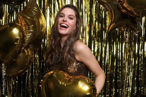 Happy woman in festive outfit holding gold balloons.