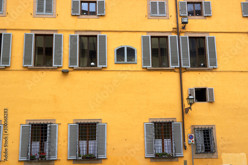 Facade of house with yellow - orange wall, windows with shutters in Firenze, Italy.