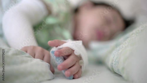 Little asian girl was lying ill in bed at the hospital, Close-up children hand intravenous treat with the brine at hospital. Real time handheld shot 4K	