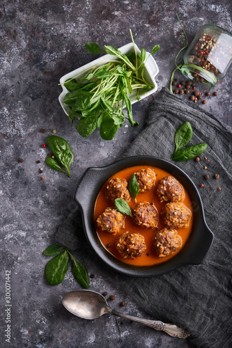 homemade meatballs with tomato sauce and spinach served in a plate on a dark stone table Top view