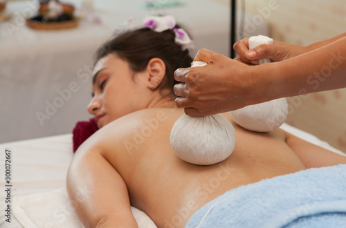 Asian woman getting thai massage with hot herbal compress on the bed at spa.