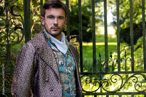 Portrait of handsome gentleman dressed in vintage costume standing in stately home courtyard with railings in background