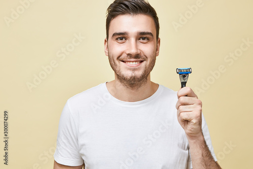 Masculinity, beauty and skin care concept. Portrait of handsome young male with bristle looking at camera with broad smile holding shaving stick, going to shave beard in the morning before work