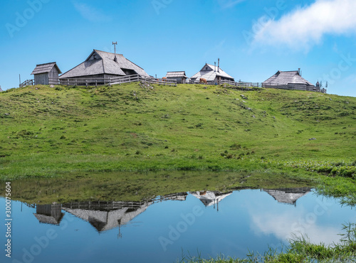 Traditional wooden cottages in village on Velika planina (Big Pasture Plateau) and reflections in water, Slovenia
