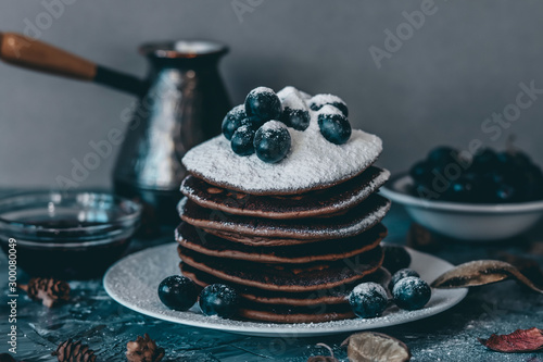 Pancakes on a white plate in powdered sugar with grapes on a gray background.
