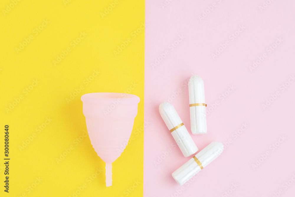 pink menstrual Cup and tampons on colorful pink and yellow background. woman period concept.