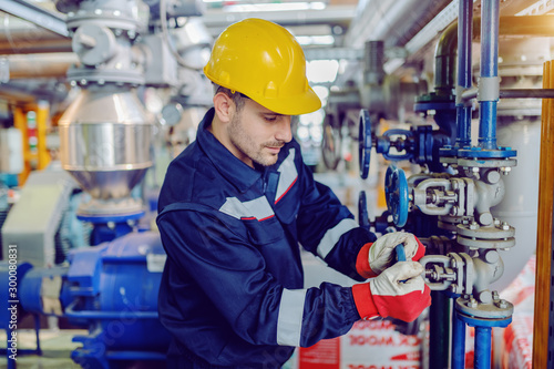Fotografía Dedicated hardworking worker in protective working clothes and with helmet on head screwing valve while standing in factory