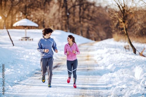 Happy smiling caucasian couple in sportswear running in nature while looking at each other. Winter time. © dusanpetkovic1