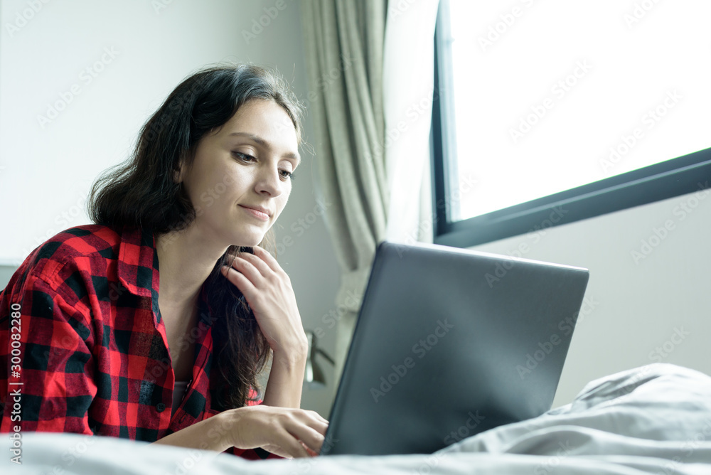 Beautiful woman working on a laptop with smiling and lying down on the bed at a condominium in the morning. Beautiful woman working on a laptop with smiling and lying down on the bed at a condominium in the morning.