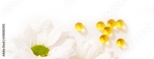 Long banner Yellow vitamins in capsules close-up on a background of chamomile flowers. natural medicine, homeopathic pills on white background. copy space. photo