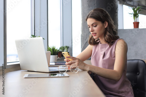 Beautiful business woman is using her smartphone with smile while sitting at her working place