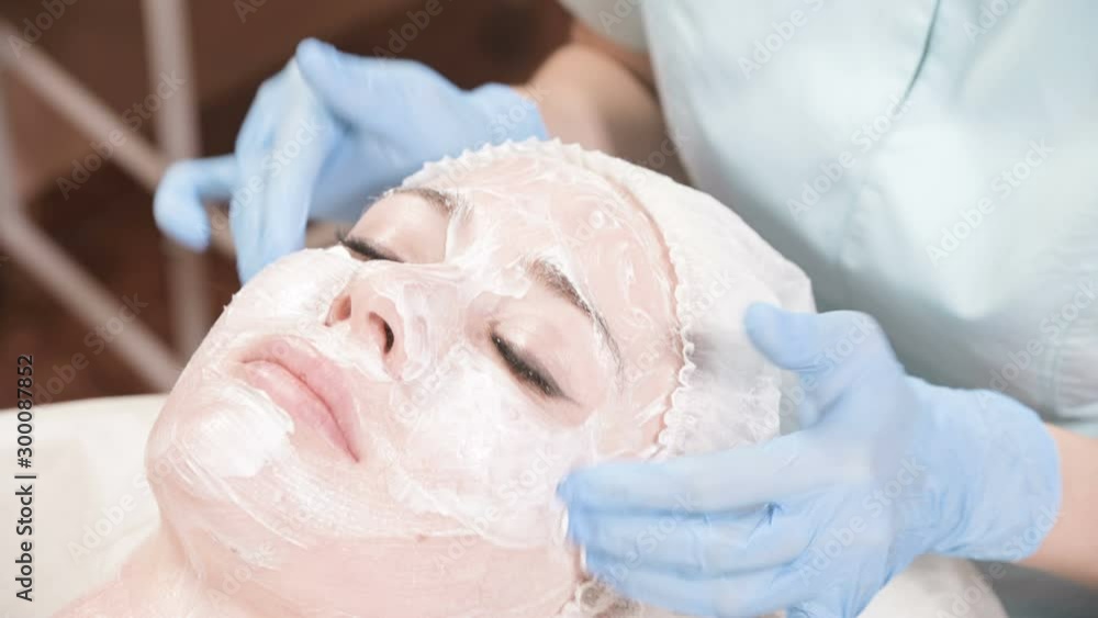 The girl a cosmetologist performs the procedure of cleansing and moisturizing the skin. Apply a mask with a special brush for a woman's face. Caring for your skin. The girl a cosmetologist performs the procedure of cleansing and moisturizing the skin. Apply a mask with a special brush for a woman's face. Caring for your skin.
