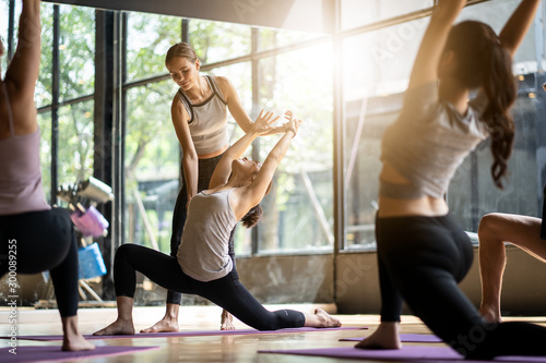 Obraz Grupa wieloetnicznego ludzi uczących się jogi w klubie fitness. Nauczycielka instruktorka rasy kaukaskiej i dostosuj prawidłową pozę do uczennicy z Azji z przodu, podczas gdy inni ją śledzą.
