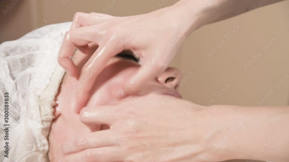 Close-up Spa facial Massage. Girl professional massage therapist does a relaxing facial massage to an attractive client of a spa salon Close-up Spa facial Massage. Girl professional massage therapist does a relaxing facial massage to an attractive client of a spa salon