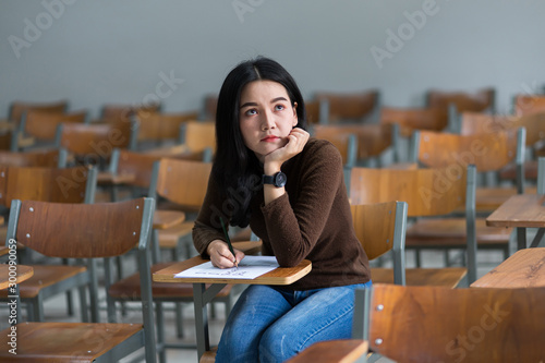 Teenager university student concetrating and writing examination in classroom seriousely. Female university student study alone in classroom with wooden chairs seriousely. photo