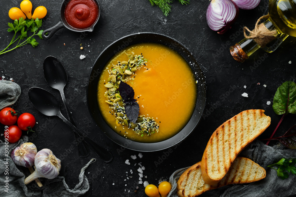 Pumpkin soup with pumpkin seeds in a black plate on a black background. Top view. Free space for your text.