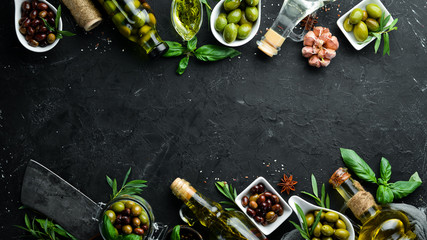 Olive oil, olives and spices on a black stone background. Top view. Free space for your text.