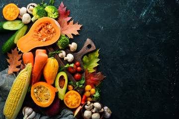 Autumn vegetables on a black stone background: Pumpkin, tomatoes, corn, cucumber, onion, carrot. Autumn food. Top view. Free copy space.