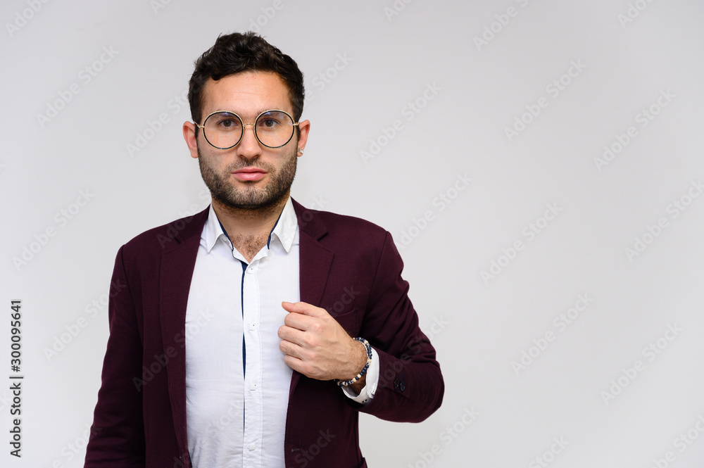Men's fashion concept. Portrait of a handsome male model in glasses shows hands wearing a dark jacket, posing on a gray background. Black hair. Close Studio Shot Men's fashion concept. Portrait of a handsome male model in glasses shows hands wearing a dark jacket, posing on a gray background. Black hair. Close Studio Shot