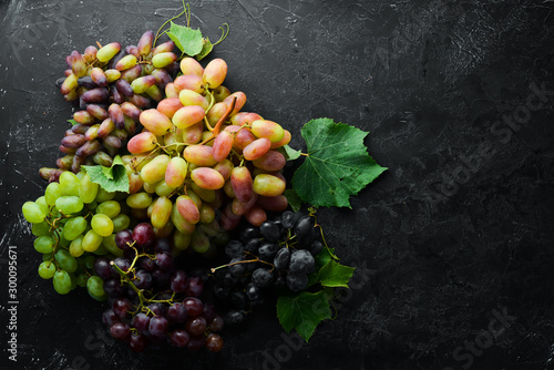 Fresh grapes with leaves on a black stone table. Top view. Free space for your text.