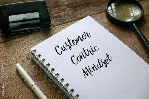 Photography Top view of magnifying glass,pen and notebook written with Customer Centric Mindset on wooden background