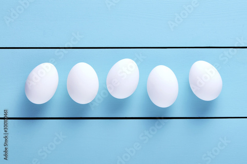 Fototapeta Naklejka Na Ścianę i Meble -  Fresh white farm eggs lined up in a row on blue wooden table with copy space