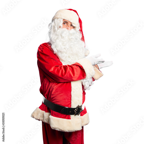 Middle age handsome man wearing Santa Claus costume and beard standing pointing aside with hands open palms showing copy space, presenting advertisement smiling excited happy